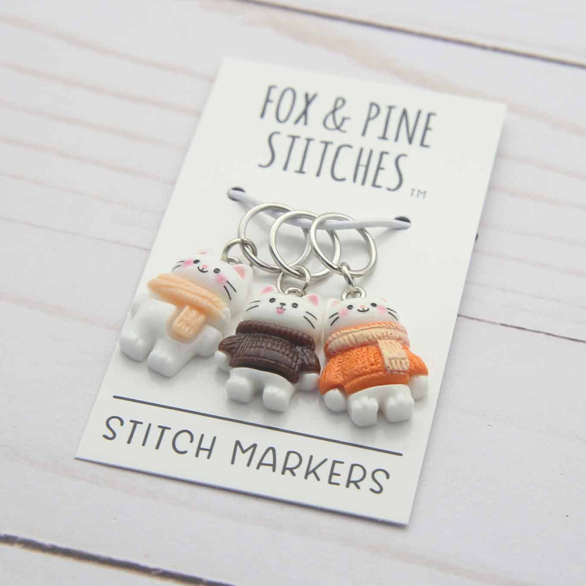 Set of stitch markers on a card with 'Fox & Pine Stitches' branding on a wooden surface.