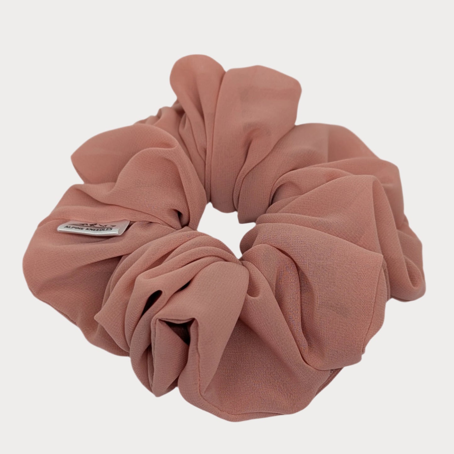 Pink scrunchie with a brand label on a white background