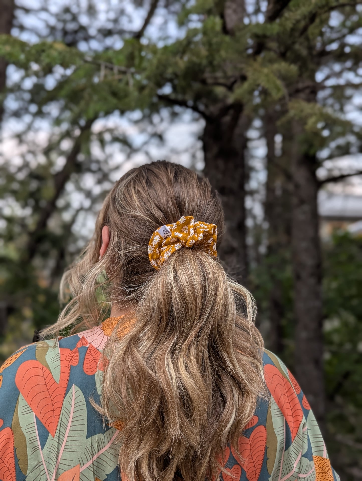 Person with a scrunchie in their hair, standing outdoors with trees in the background