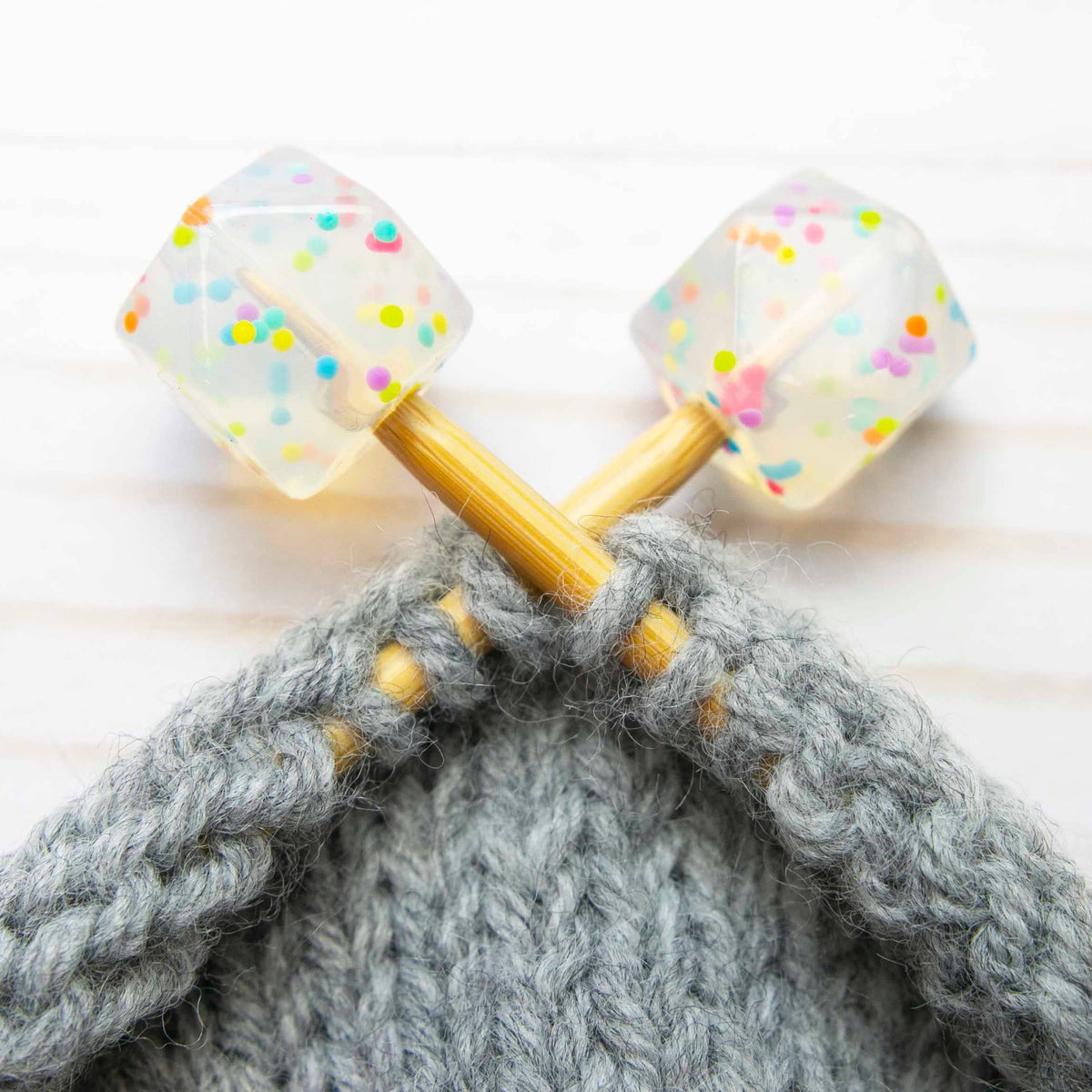 Knitting needles with colorful stitch stopper on a gray knitted fabric.