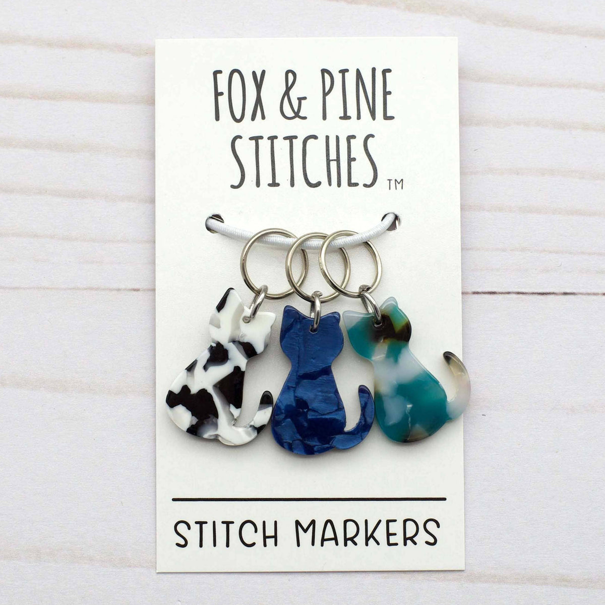 Set of stitch markers with a 'Fox & Pine Stitches' card on a wooden surface
