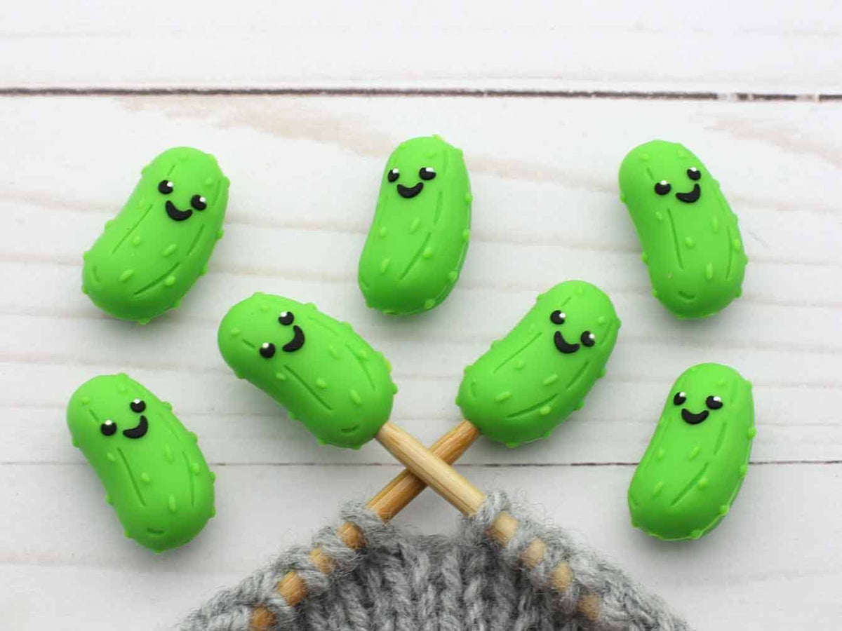 Green pickle-shaped stitch stoppers on knitting needles