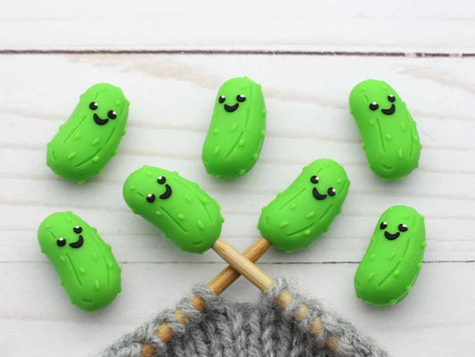 Green pickle-shaped stitch stoppers on knitting needles