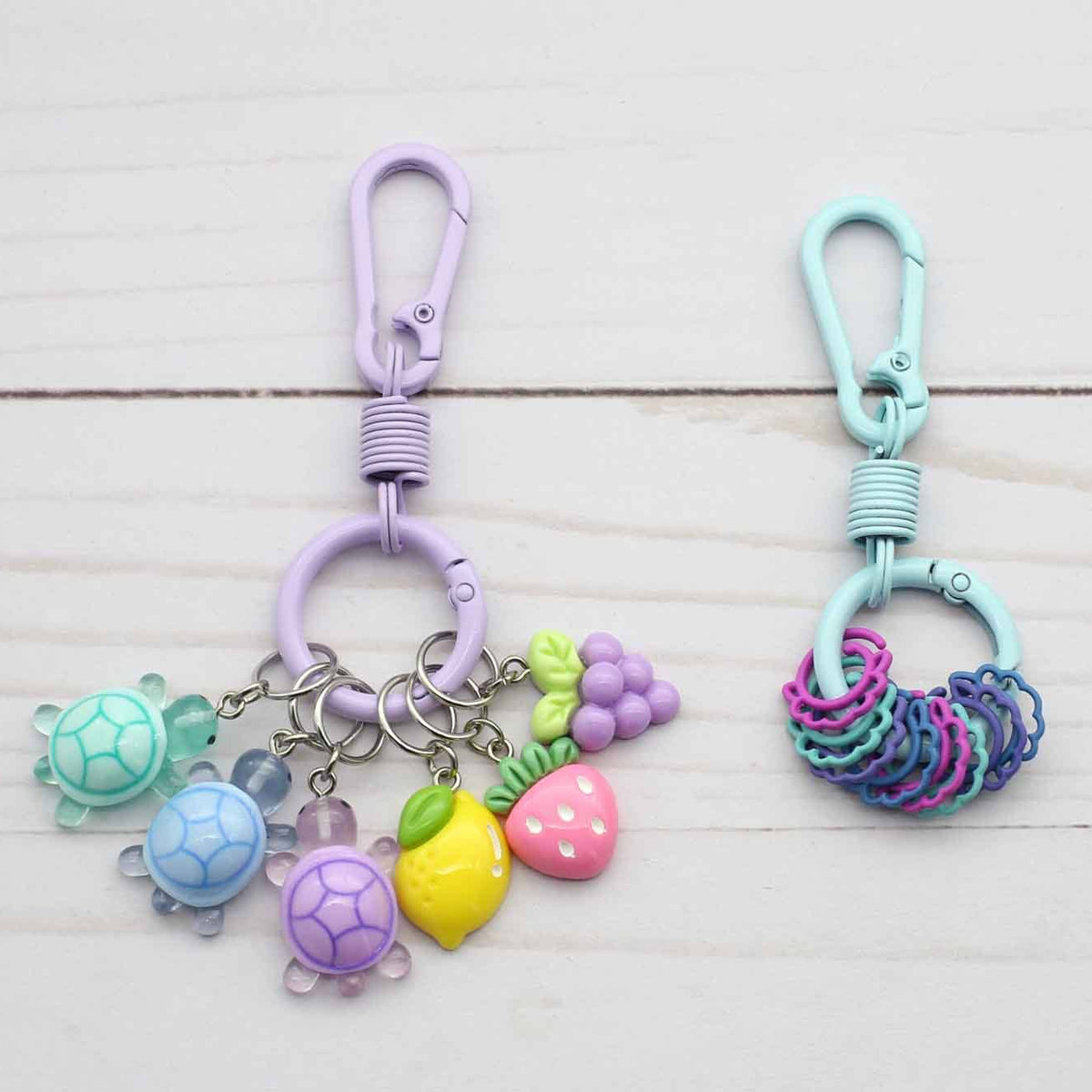 Two colorful keychains with turtle, fruit, and interlocking ring designs on a light wooden surface.
