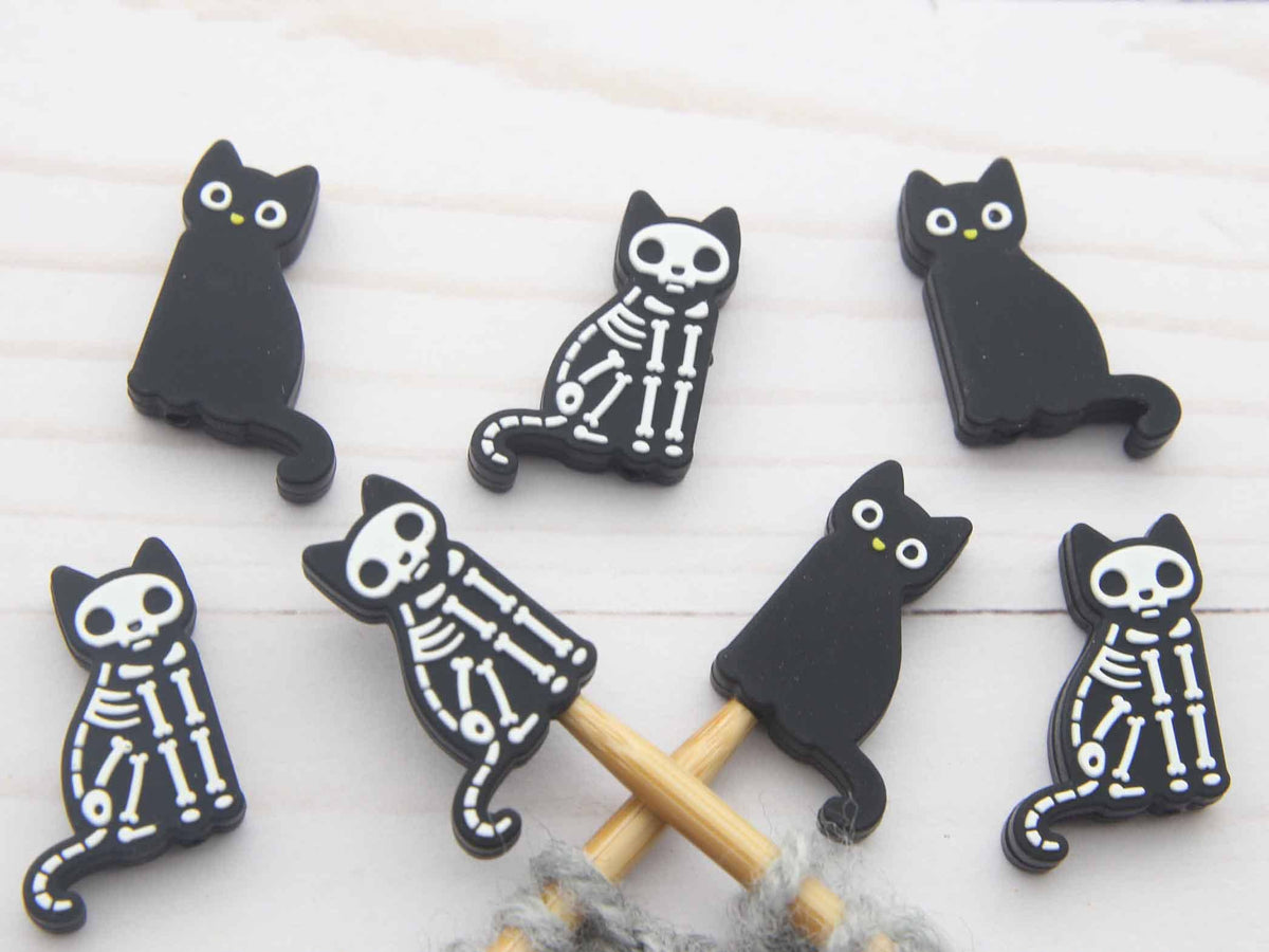 Six black cat-shaped stitch stoppers on knitting needles