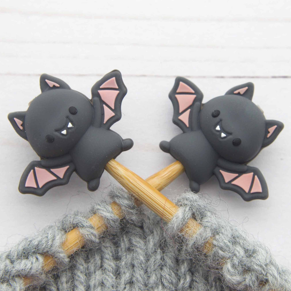Two black bat-shaped stitch stoppers on knitting needles