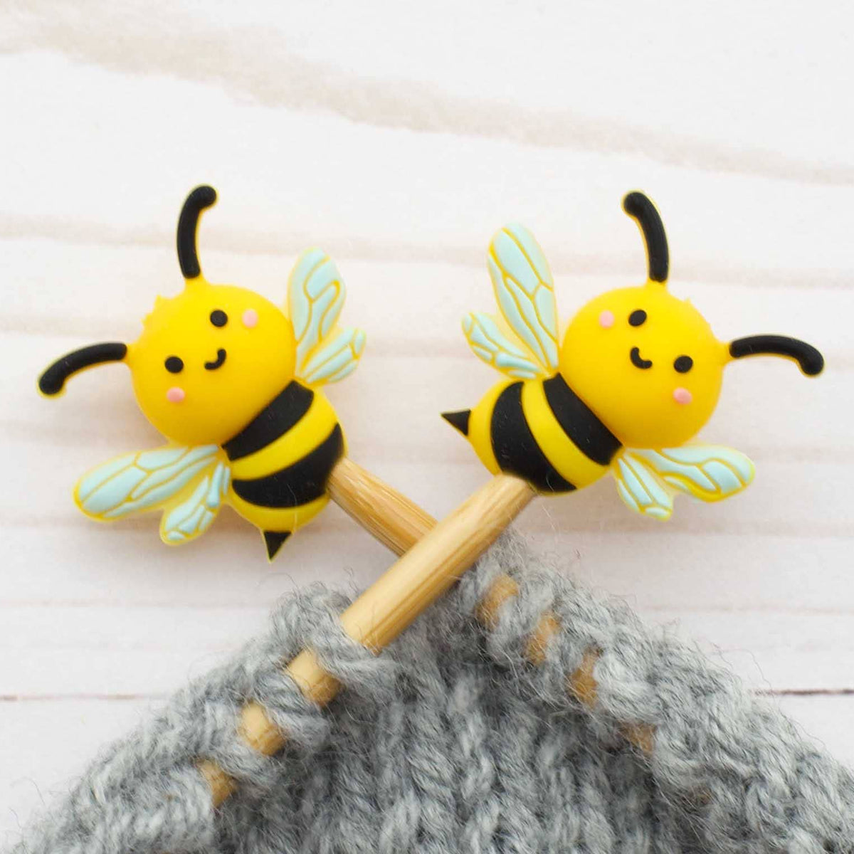 Two bee-shaped stitch stoppers on knitting needles
