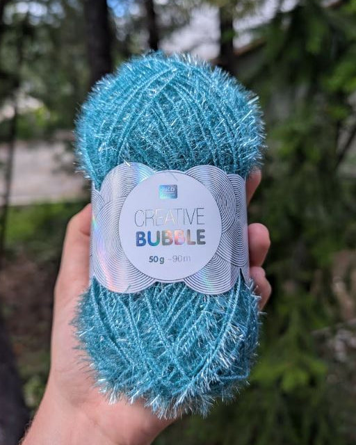 Blue yarn ball with a label held in front of a blurred natural background