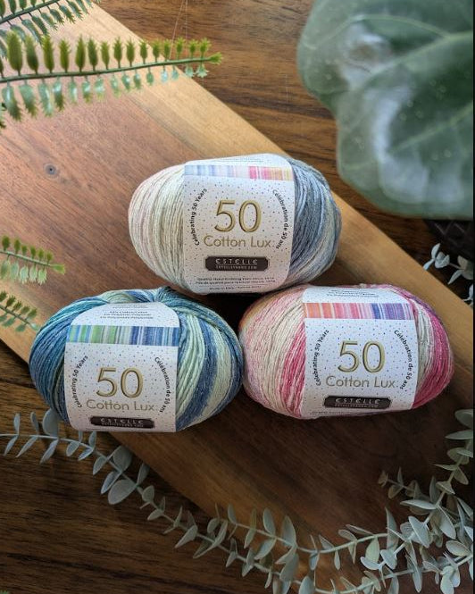 Three skeins of colorful yarn on a wooden surface with greenery.