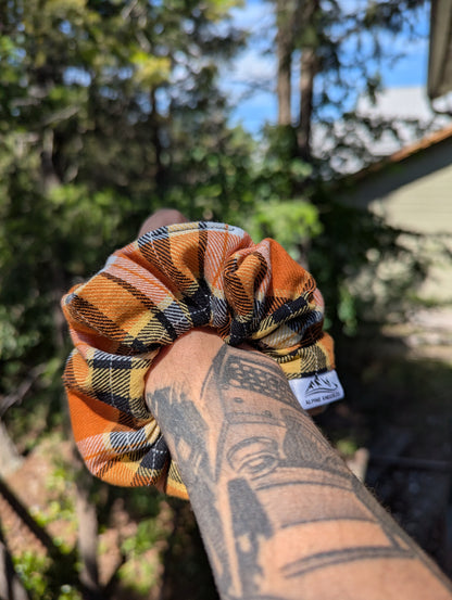 Plaid scrunchie held by a tattooed hand with a blurred outdoor background
