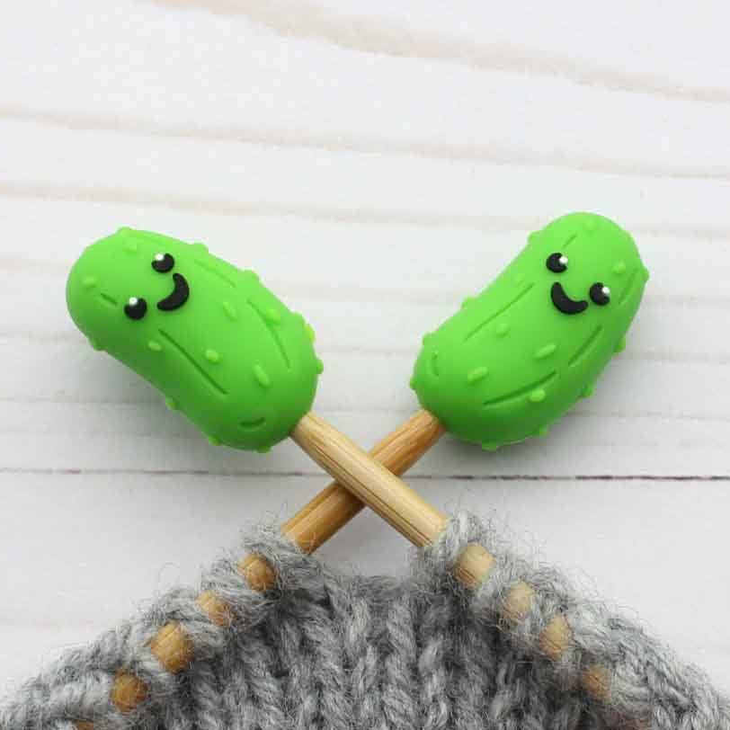 Two green pickle-shaped stitch stoppers on knitting needles