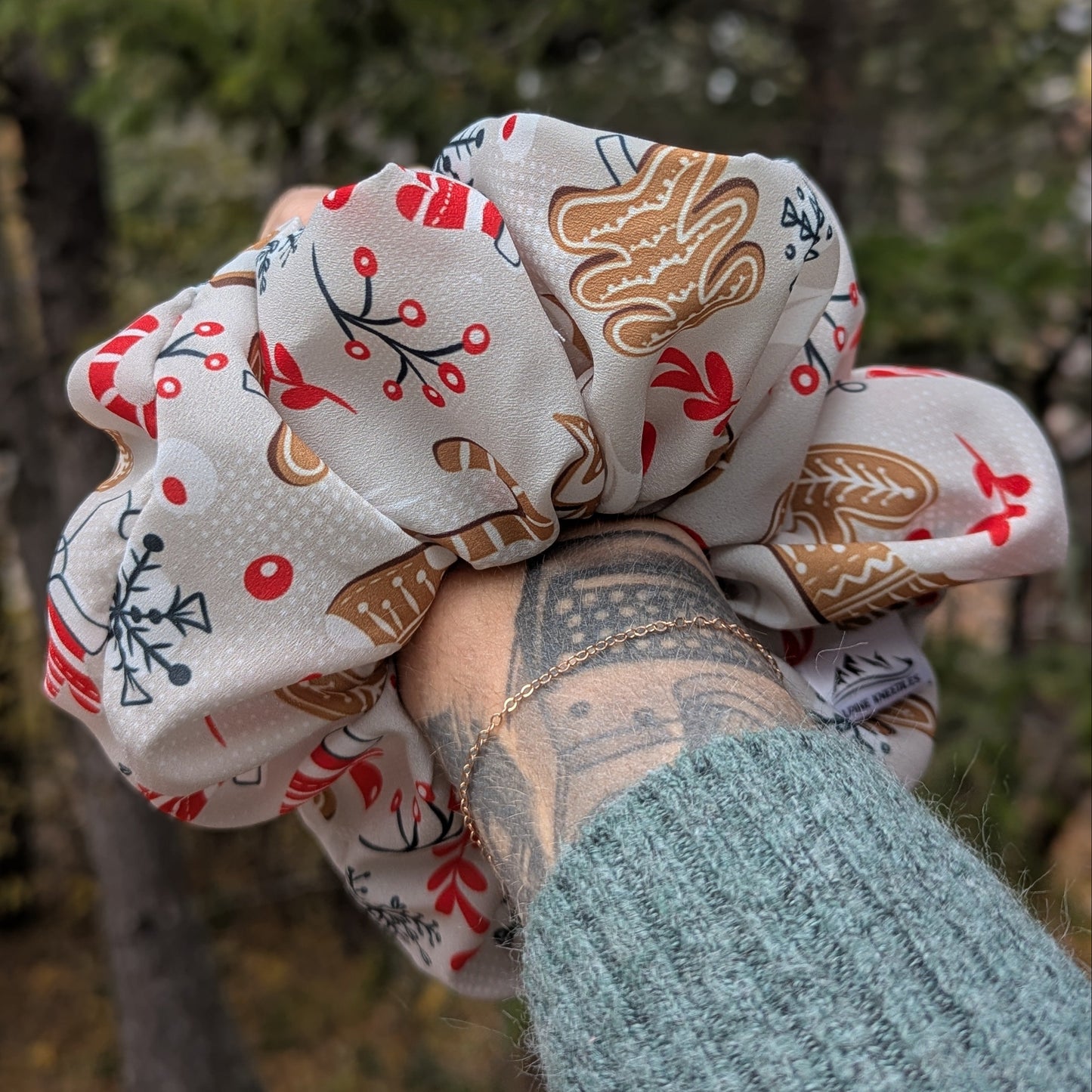 Two fabric scrunchies with gingerbread man and snowflake patterns held against a blurred natural background.