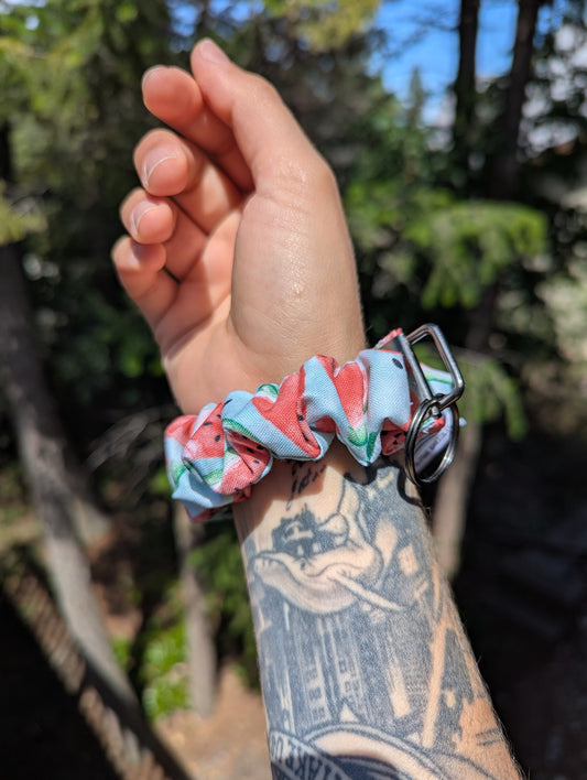 Hand wearing a colorful scrunchie with a tattooed arm against a natural background