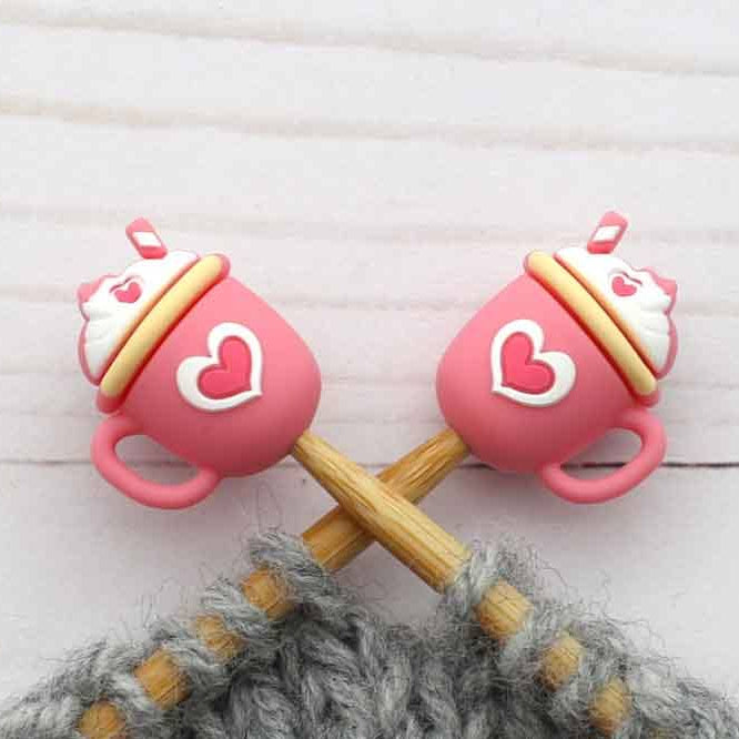 Pink cup-shaped knitting stitch stoppers with wooden needles on a textured surface
