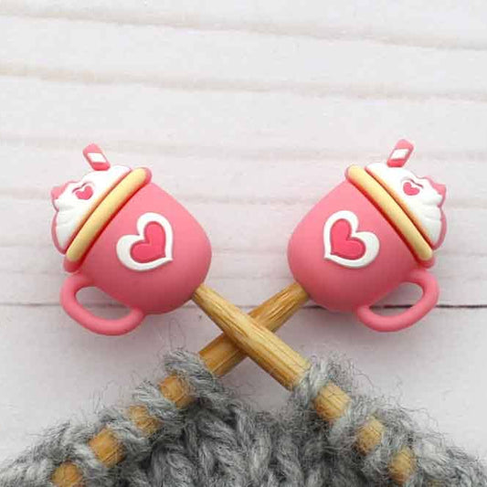 Pink cup-shaped knitting stitch stoppers with wooden needles on a textured surface