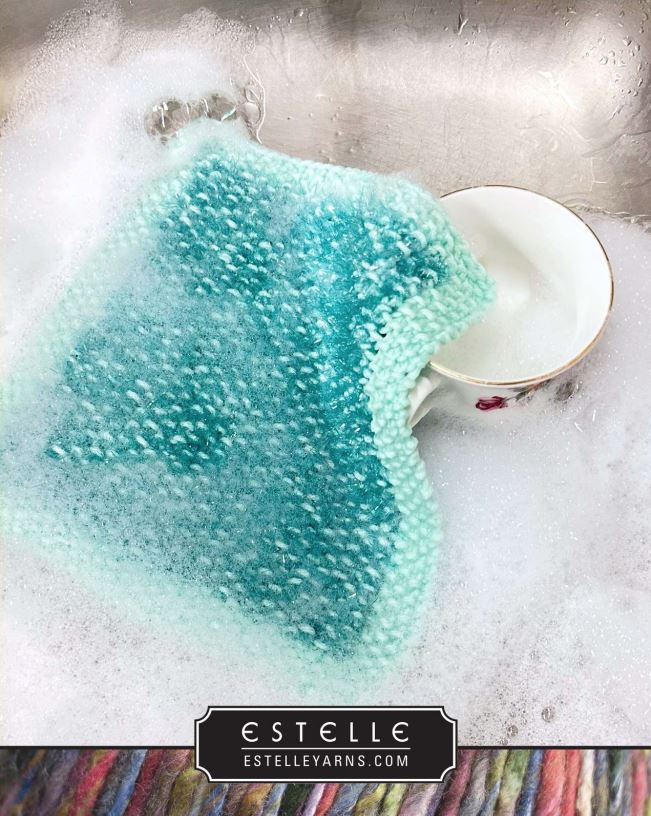 Knitted fabric with a gradient of blue and green colors in a sink with soapy water, featuring the brand 'Estelle'.