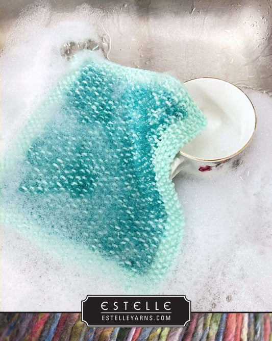 Knitted fabric with a gradient of blue and green colors in a sink with soapy water, featuring the brand 'Estelle'.