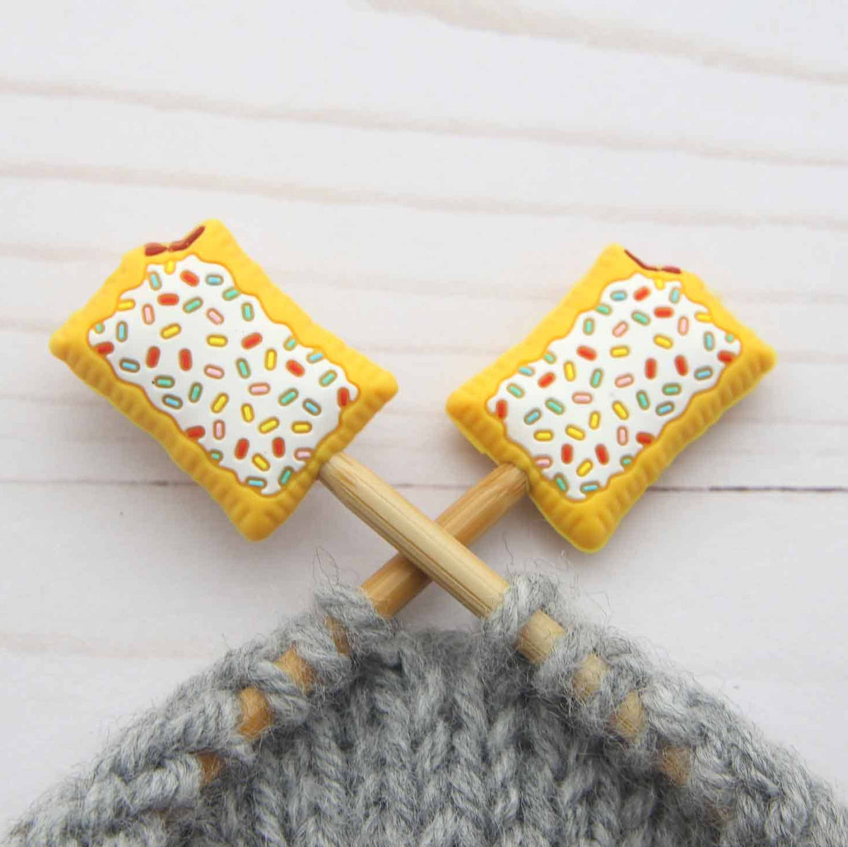 Two toaster pastries with sprinkles stitch stoppers on knitting needles