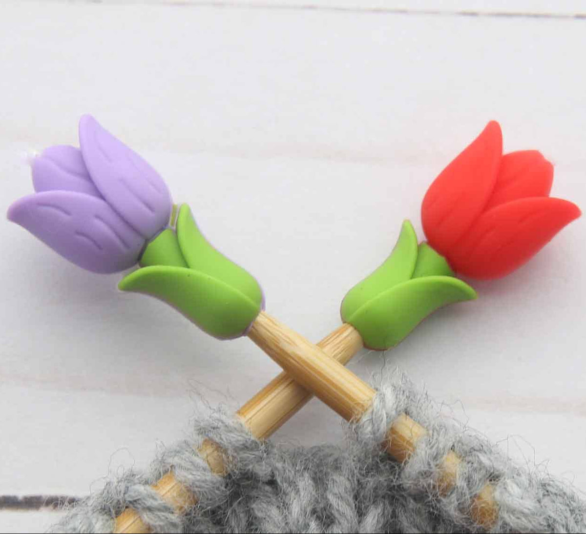 Knitting needle tips with colorful tulip-shaped stitch stoppers on knitting needles