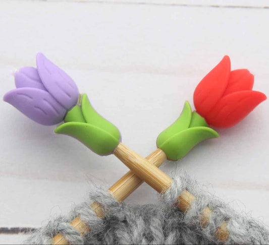 Knitting needle tips with colorful tulip-shaped stitch stoppers on knitting needles