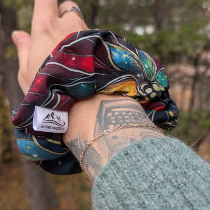 Colorful scrunchie with a visible brand logo held by a person outdoors.