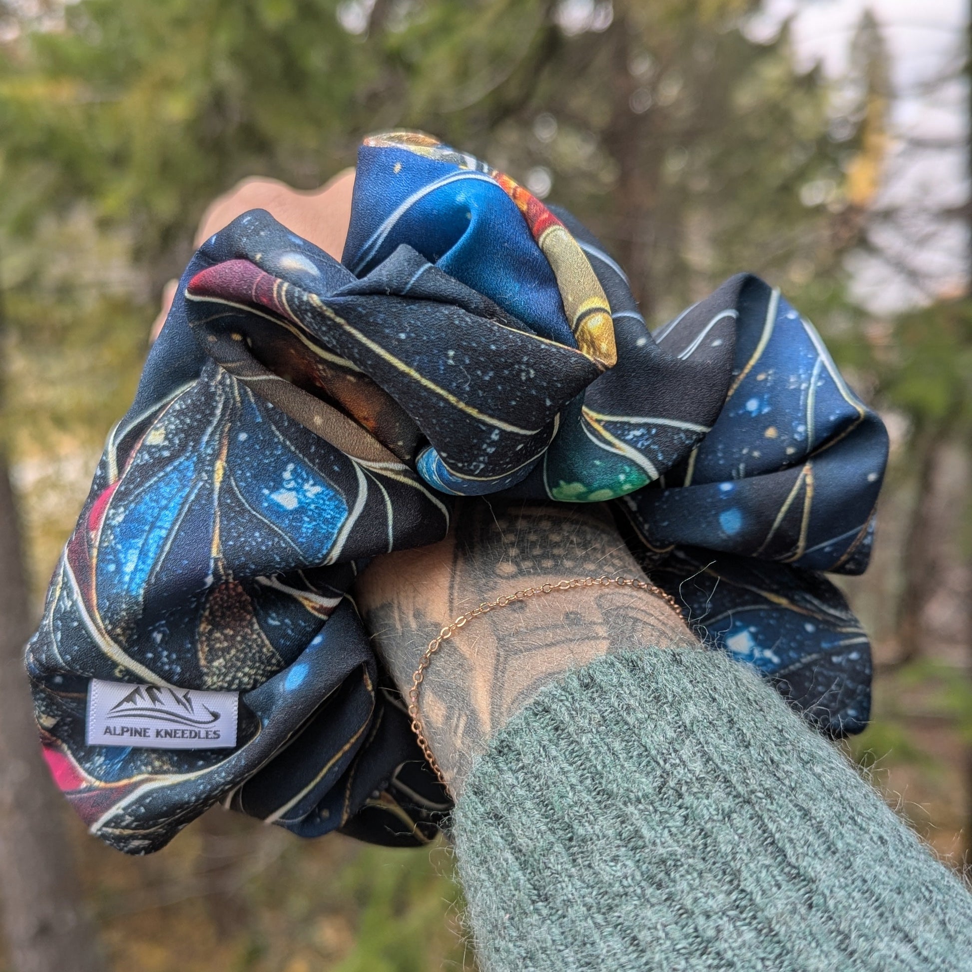 Hand holding a colorful scrunchie with a blurred natural background