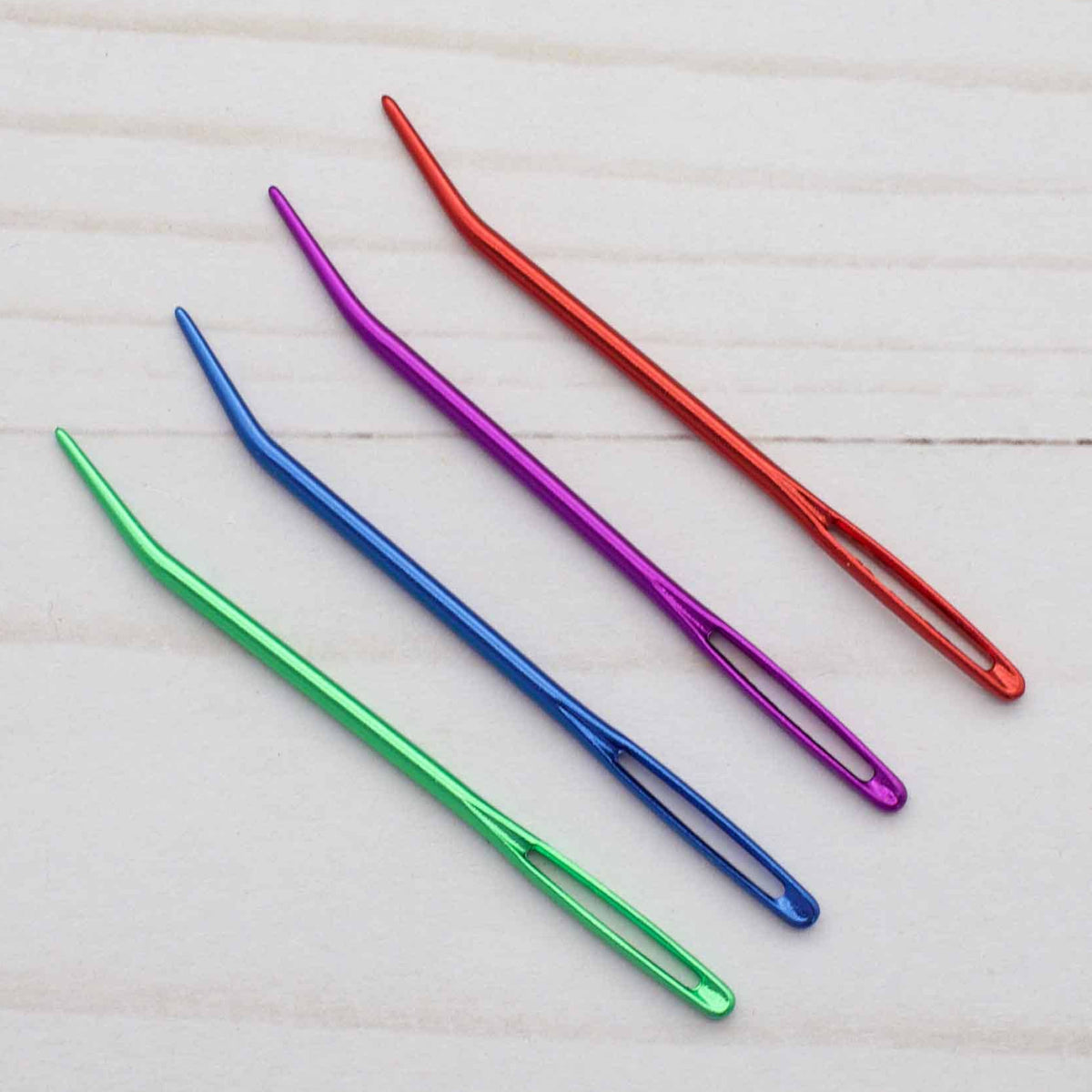 Set of colorful darning needles on a light wooden surface