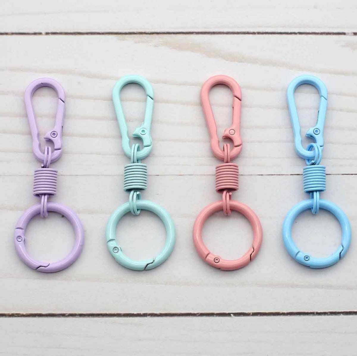 Four colorful keychains with spring-loaded carabiners on a wooden surface.